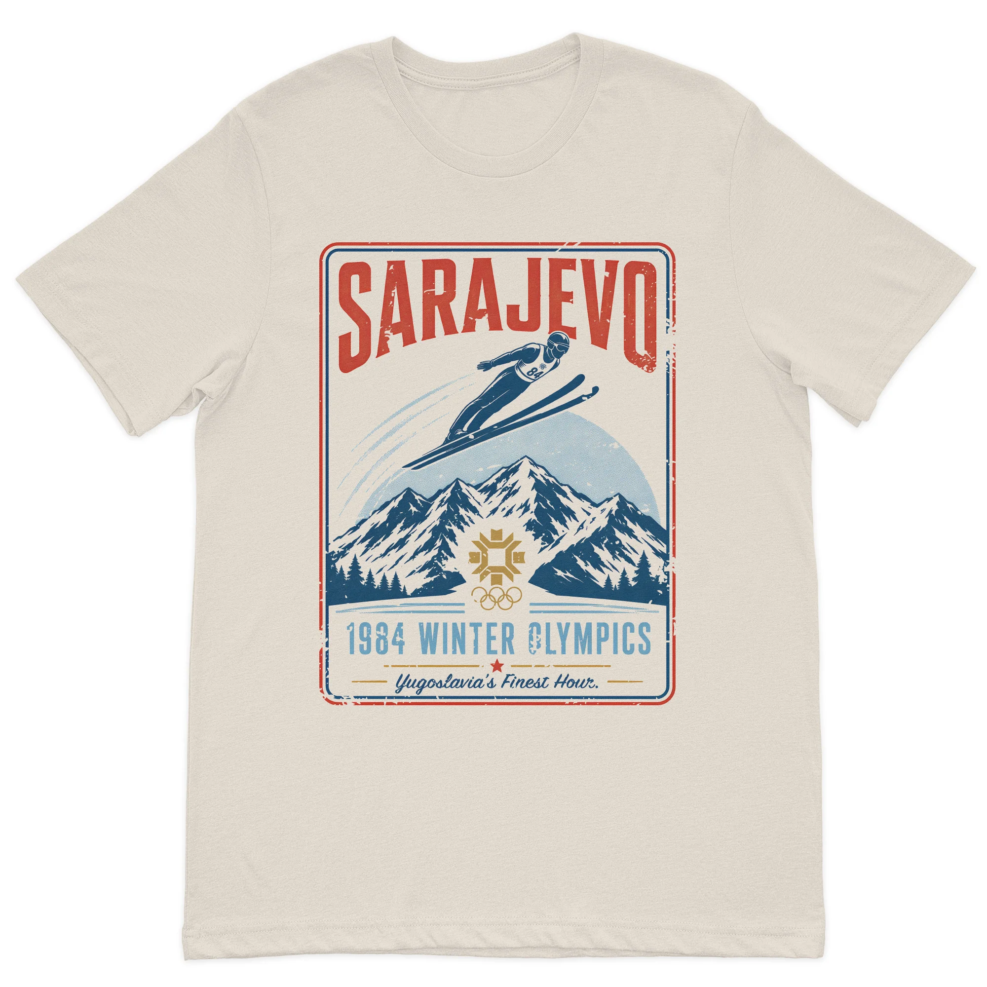 Vintage Sarajevo 1984 winter sports inspired graphic t-shirt featuring mountain scenery and a retro travel poster design on a premium sand cotton t-shirt.